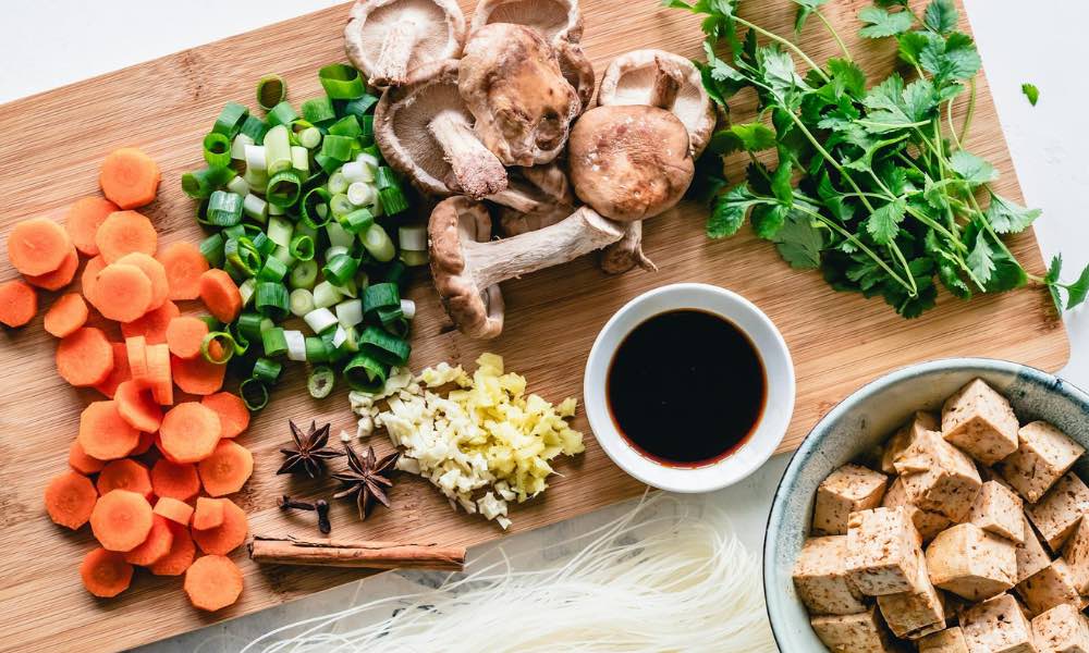 Overhead view of a cutting board covered with chopped vegetables, spices, herbs, sauces, and tofu