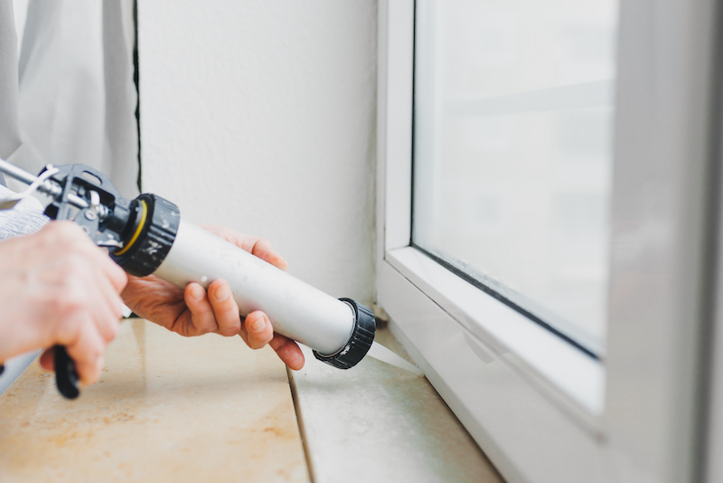 Someone holding a caulk gun and caulking a window