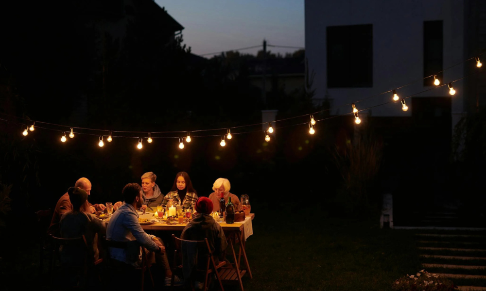 A family sitting at a table at night with Edison-bulb string lights hanging overhead.