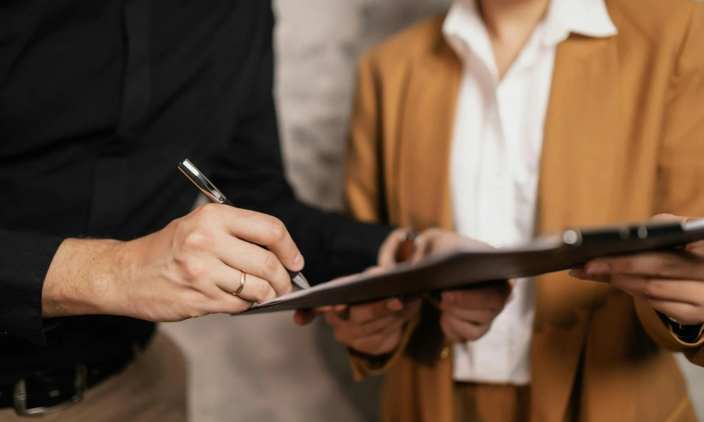 Person holding a clipboard while another person signs a paper on it.